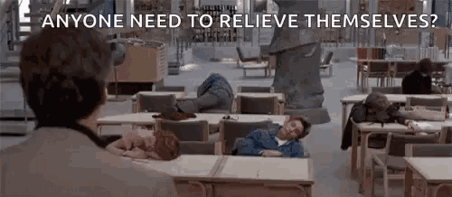 a man is standing in a library looking at people sleeping at tables and chairs .