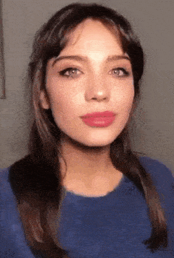 a close up of a woman 's face with a blue shirt and pink lipstick .