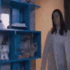 a woman in a white dress is standing in front of a blue bookshelf .