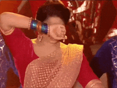 a woman in a red blouse and a pink saree is covering her face with her hand .