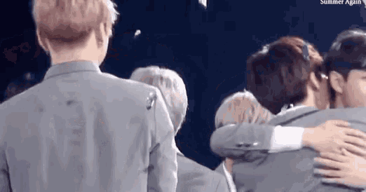 a group of men in suits are hugging each other on a stage .