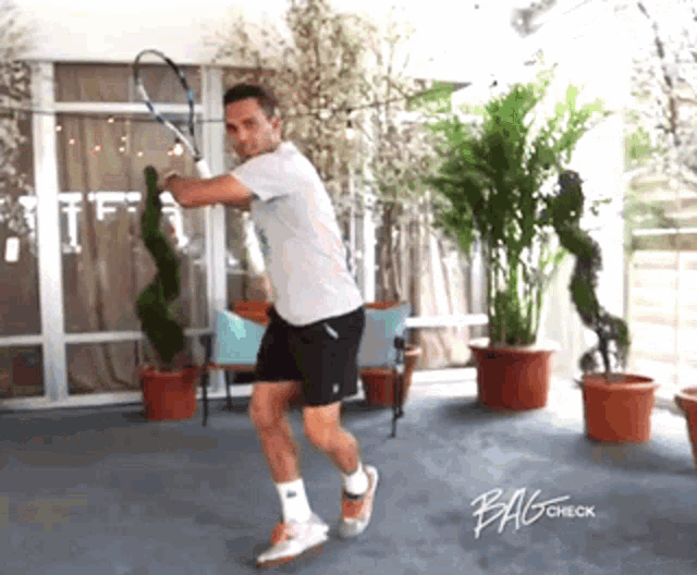 a man is swinging a tennis racquet in a room with bagcheck written on the bottom