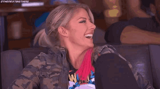 a woman is sitting on a couch laughing and wearing a camouflage jacket .