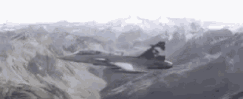 a fighter jet is flying over a snowy mountain .