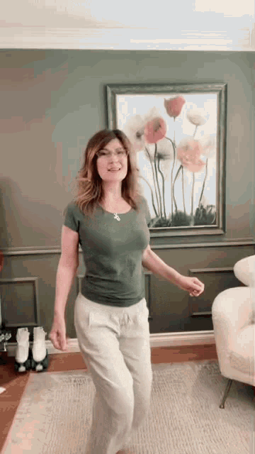 a woman in a green shirt and white pants is dancing in a living room .