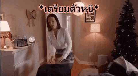 a woman is standing in a living room with a christmas tree .