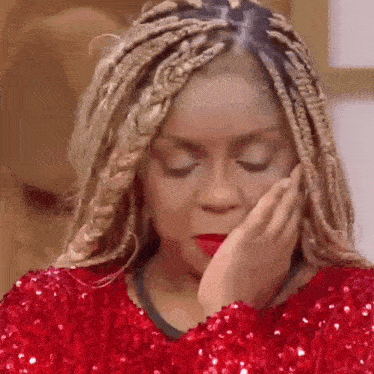 a woman with braids is wearing a red sequined shirt and covering her face with her hand .