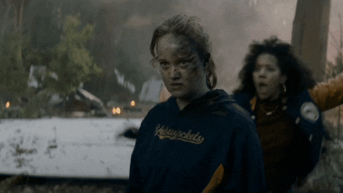 a woman wearing a yellowjackets sweatshirt stands in a forest