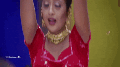a woman in a red dress and gold jewelry is holding her hair up .