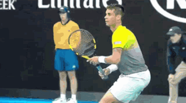a man is holding a tennis racquet on a court in front of an emirates sign