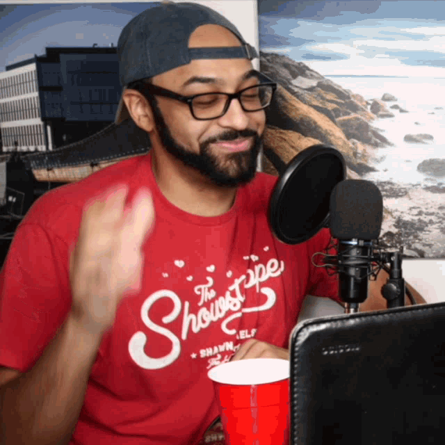 a man wearing a red shirt that says the showstripe is sitting in front of a microphone