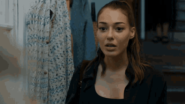 a woman in a black shirt is standing in front of a wall with clothes hanging on it