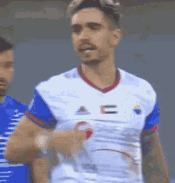 a man in a white and blue soccer uniform is standing on a field .