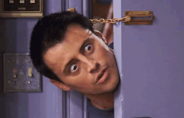 a man is peeking out of a door with his eyes wide open and a chain around his neck .