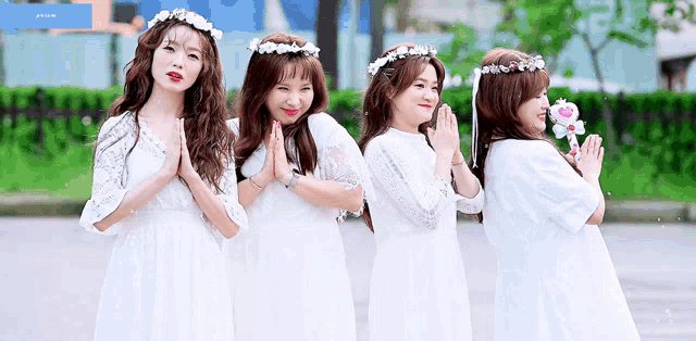 four girls wearing white dresses and flower crowns are posing for a picture together .