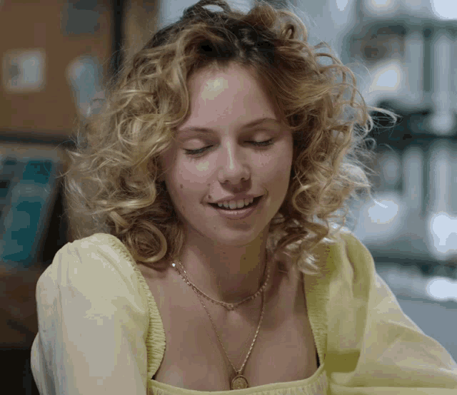 a woman with curly blonde hair wearing a yellow top and a gold necklace