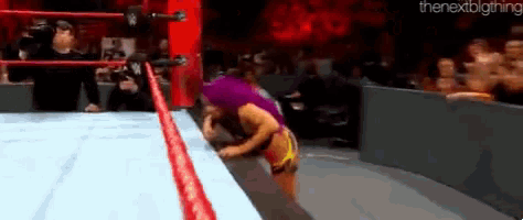 a female wrestler is standing on the edge of a ring .