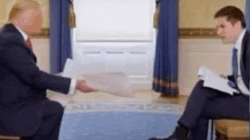 a man in a suit and tie is giving a piece of paper to another man in a room .
