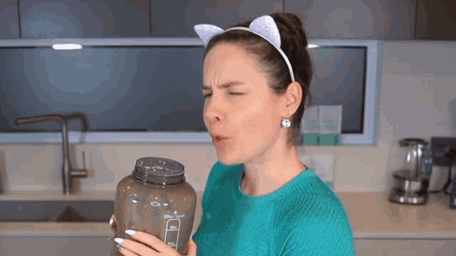 a woman wearing a cat ear headband is holding a bottle that has a measurement of 1 liter on it