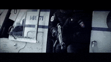 a man holding a gun in front of a helicopter with the number mm71 on the side