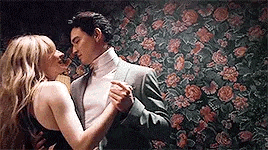a man and a woman are dancing together in front of a floral wallpaper .