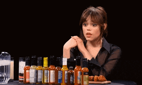 a woman is sitting at a table with bottles of hot sauce and the words " fuck that " behind her