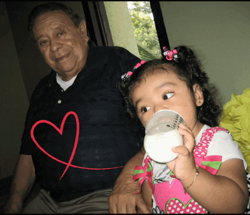 a little girl is drinking milk from a bottle with a heart drawn on it