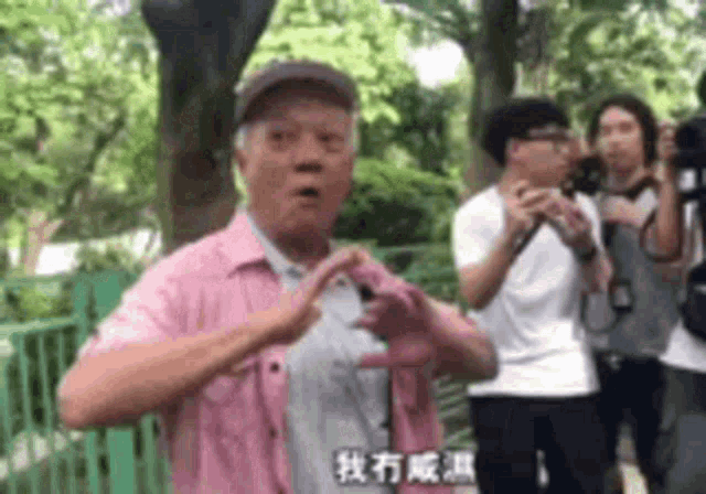 a man in a pink shirt is making a heart shape with his hands while standing in front of a group of people .