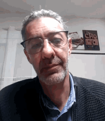 a man with glasses and a beard is standing in front of a wall with a sign that says cho