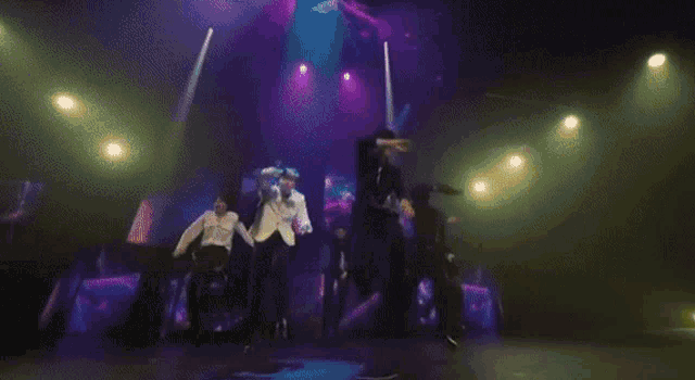 a group of men are dancing on a stage with a purple light coming from the stage .