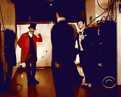 a man in a top hat is standing in a dark room with two other men