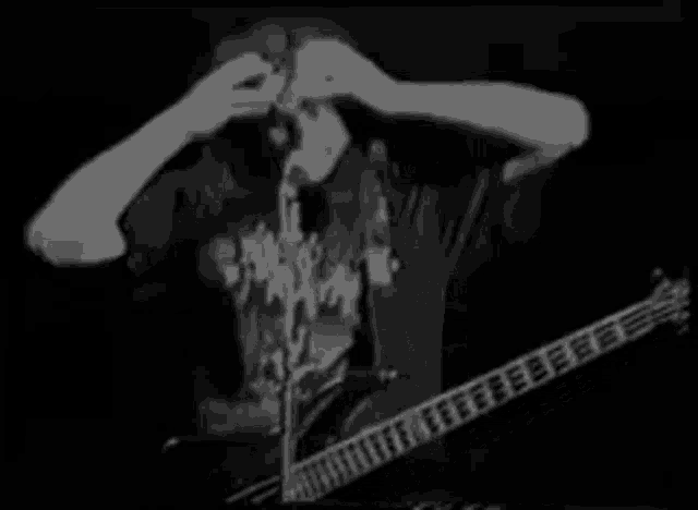 a man is playing a guitar and singing into a microphone while holding his head .