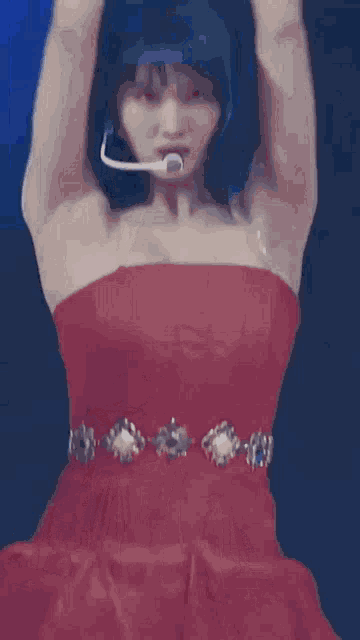a woman in a red dress is dancing on a stage with her arms up .