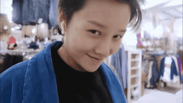 a woman wearing a blue jacket and earrings is smiling