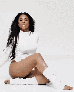 a woman in a white bodysuit is kneeling on the floor with her legs crossed .