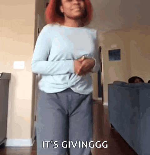 a woman with red hair is standing in a living room with the words it 's givinggg written on the bottom