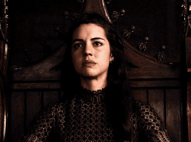 a woman is sitting in a wooden chair with a crown on her head