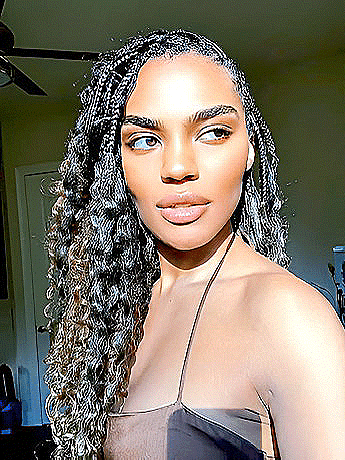 a woman with long curly hair is standing in a room with a ceiling fan in the background .