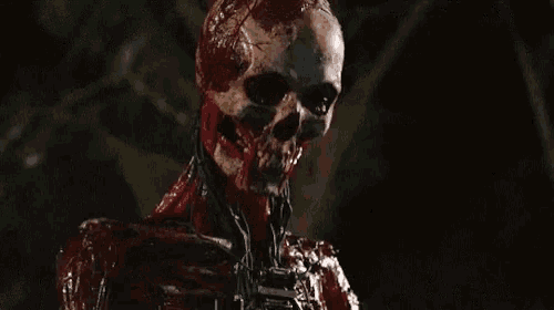 a bloody skeleton with a chain around its neck is standing in the dark and looking at the camera .