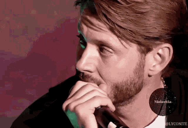 a man with a beard is holding his hand to his chin and looking to the side .