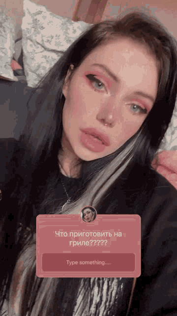 a woman with black hair and pink eye shadow is looking at the camera with a pink sticker that says type something