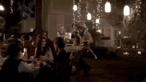 a group of people are sitting at tables in a room with lights hanging from the ceiling .