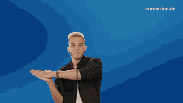 a man in a black jacket stands in front of a blue background that says eurovision.de