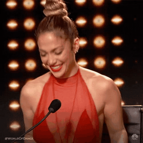a woman in a red dress is smiling while speaking into a microphone .
