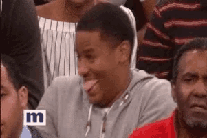 a man is making a funny face while sitting in a crowd of people .