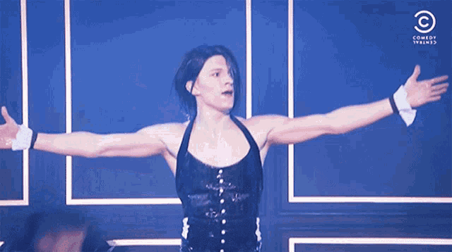 a man with his arms outstretched in front of a blue wall with comedy central in the corner