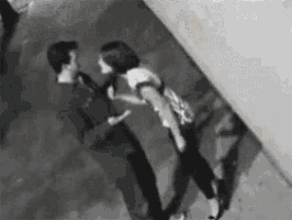 a man and a woman are standing next to each other on a sidewalk in a black and white photo .
