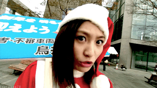 a woman wearing a santa hat stands in front of a sign with chinese writing