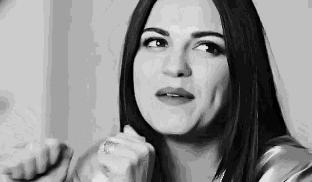 a black and white photo of a woman with a ring on her finger making a funny face .