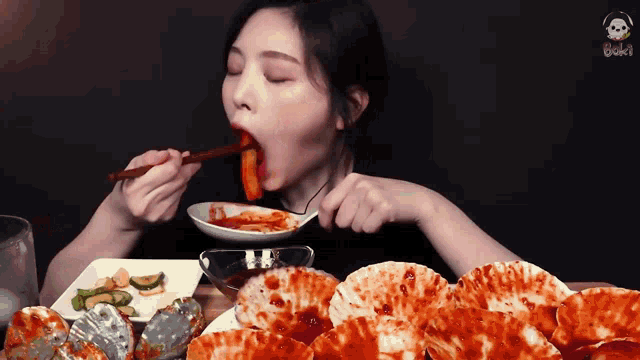 a woman is eating food with chopsticks and a plate of food in front of her